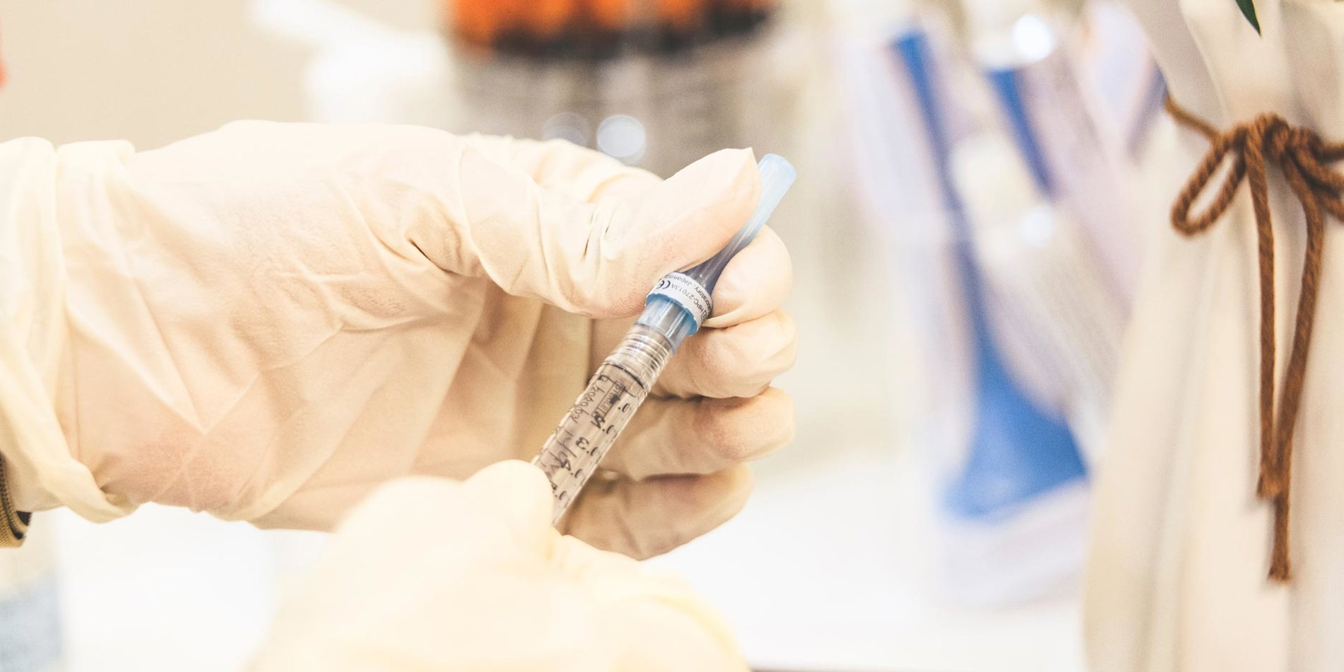 In a laboratory, gloved hands are removing the cap from a syringe.