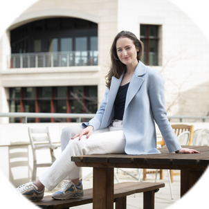 Adrienne sitting outside at a table, wearing a blue coat and smiling at the camera.