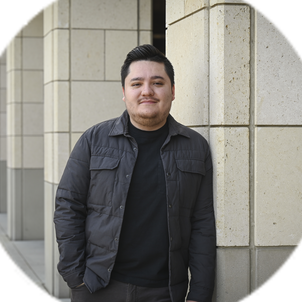 Portrait of Sebastian Fernandez, wearing a black coat and top, standing outside. 