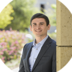 Portrait of Thomas Colburn in a gray suit, standing outside on a sunny day in the engineering quad.