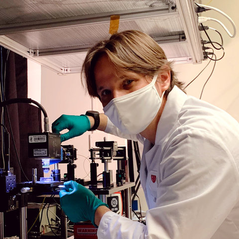 Ziv Lautman wearing a mask and gloves while working with a microscope