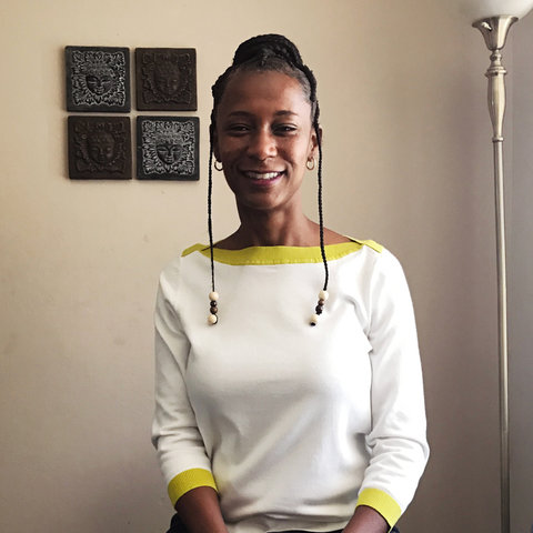 LaToya Powell smiles for her portrait in her home in front of a wall with art on it